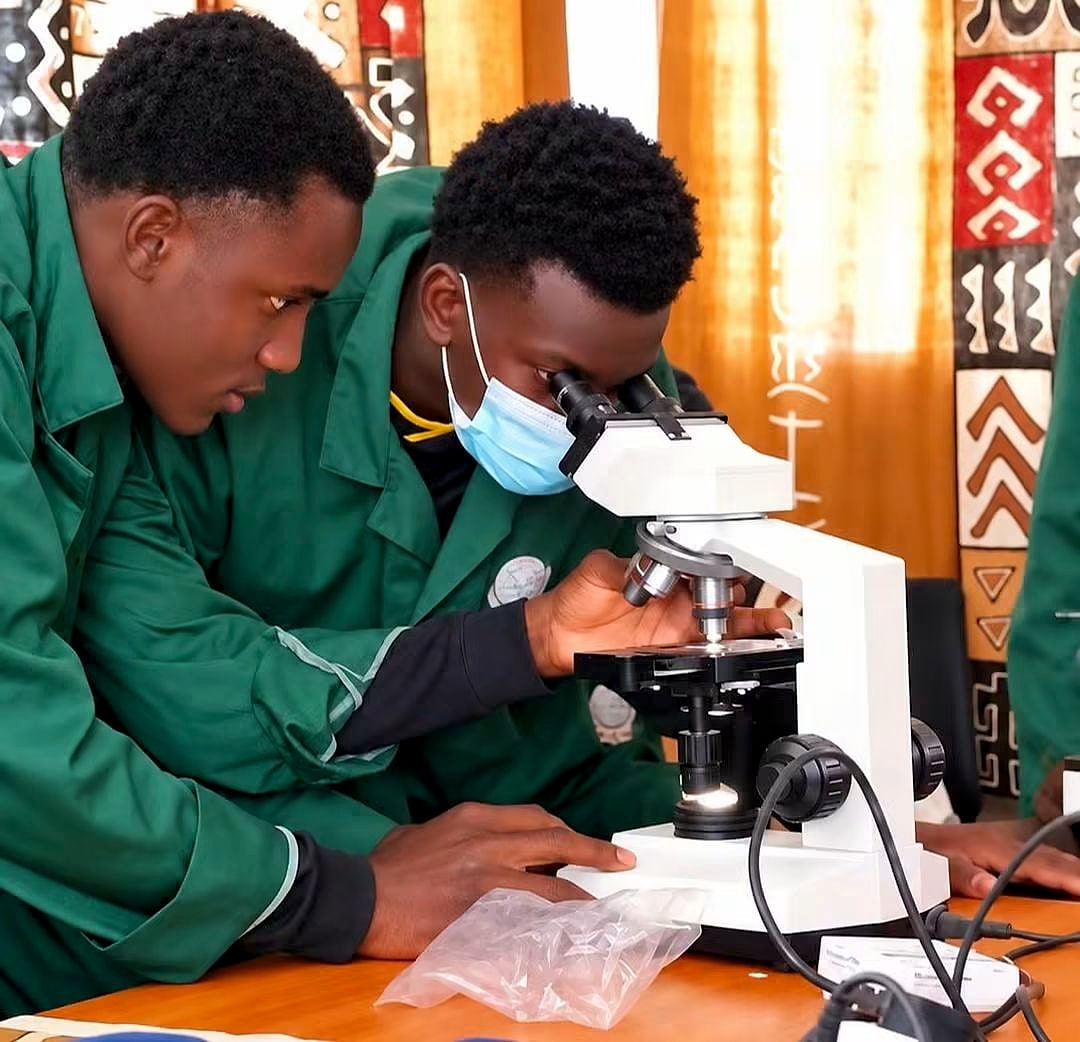 Deux étudiants en blouse verte observent un échantillon au microscope.
